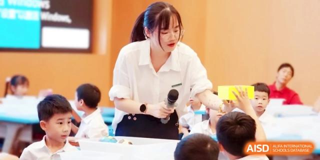A female instructor speaks into a microphone while guiding a group of young students in a classroom during an engaging science activity at Ronghaui International School.