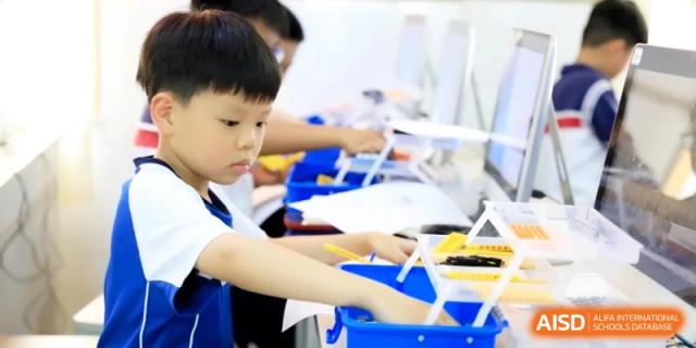 A young student focuses on constructing a small project using colorful plastic building blocks at a desk in a classroom setting at Ronghaui International School.