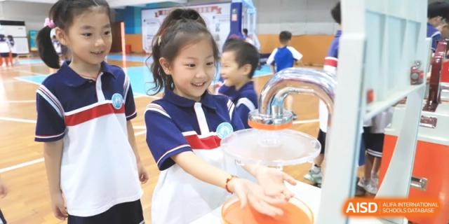 A happy young student happily interacts with a water science experiment display in a colorful activity room for interactive learning at Ronghaui International School.