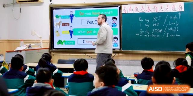 A male teacher explains a lesson about pets to a class of young students using a large interactive smartboard displaying colorful graphics at Ronghaui International School.