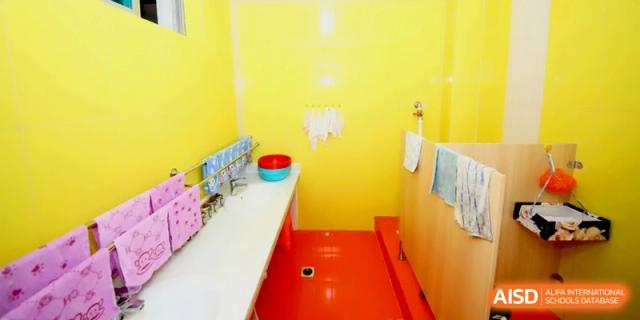A bright yellow bathroom area with small sinks, a red floor, and cleaning supplies, designed for young students to use easily at Ronghaui International School.
