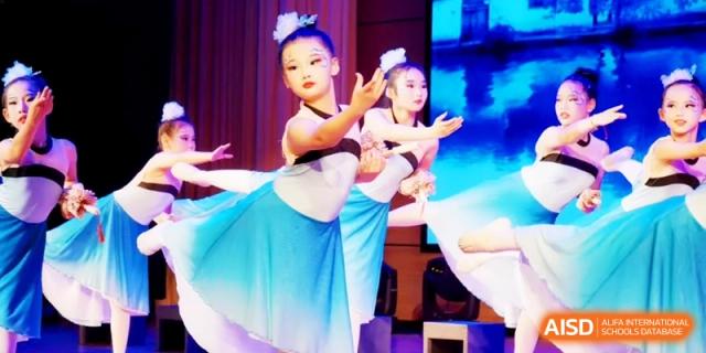 Young dancers in blue and white costumes performing a graceful routine on a brightly lit stage during a school talent show at Ronghaui International School.