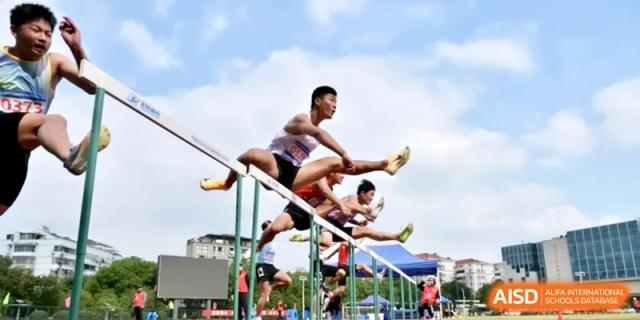 Athletes mid-action jumping over hurdles on an outdoor track during a competitive sporting event on a sunny day at Ronghaui International School.