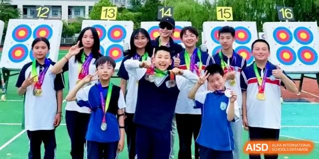 A team of young archers posing with their bows and medals in front of targets, celebrating their success in a competition at Ronghaui International School.