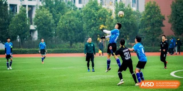 A soccer match in progress on a green field with players competing for the ball under the supervision of a referee at Ronghaui International School.