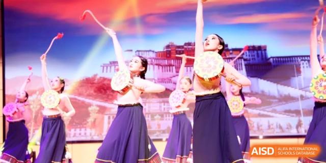 Performers in traditional attire dancing with colorful drums on a stage during a vibrant cultural festival performance at Ronghaui International School.