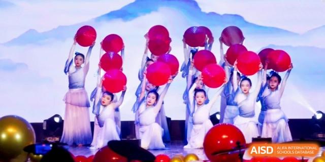 Dancers in white dresses performing a coordinated routine with red balloon props on a stage for a school assembly at Ronghaui International School.