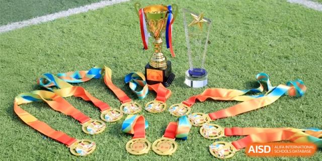 A prestigious trophy and several gold medals displayed on green grass, celebrating athletic achievements and championship victories at Ronghaui International School.