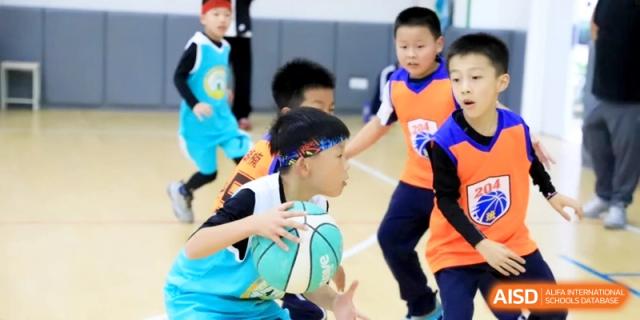 Elementary students in colorful jerseys playing a competitive game of basketball on an outdoor court during physical education at Ronghaui International School.