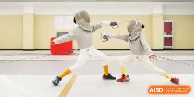Two fencers engaged in a match, wearing protective gear and aiming to score points against each other in a gymnasium at Ronghaui International School.