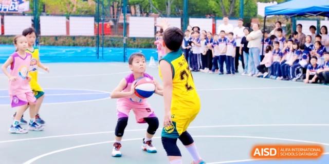 Young students in colorful jerseys playing basketball on a sunny day, focusing on teamwork and developing their sports skills at Ronghaui International School.