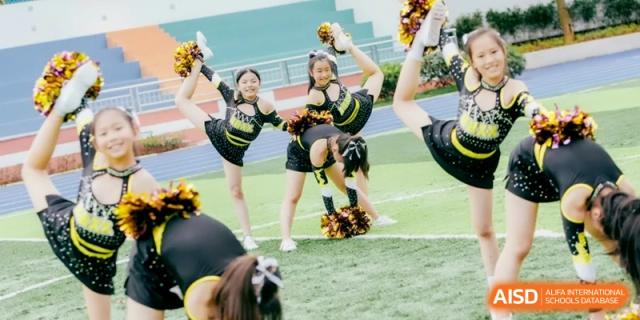 Young cheerleaders in black uniforms performing a high-energy routine on a green field, supporting their team at Ronghaui International School.