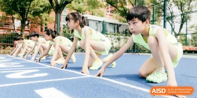 Young students practicing their sprinting stance at the start of a race on a blue running track, aiming for speed at Ronghaui International School.