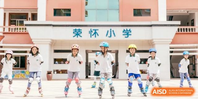 Children wearing helmets and pads rollerblading in front of the school entrance, enjoying an outdoor recreational activity at Ronghaui International School.
