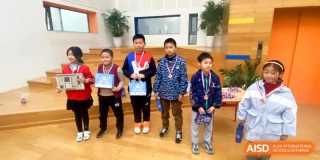 Four students wearing medals stand proudly together during a recognition ceremony at Shanghai Gold Apple Bilingual School.