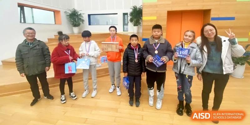 A group of students stand on a wooden stage holding awards and blue gift bags at Shanghai Gold Apple Bilingual School.