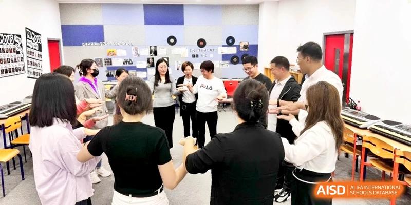 Staff members engage in a group activity, holding hands in a circle during a workshop at Shanghai Gold Apple Bilingual School.