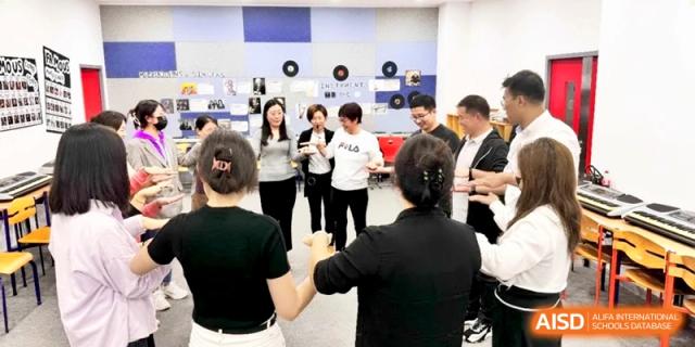 Staff members engage in a group activity, holding hands in a circle during a workshop at Shanghai Gold Apple Bilingual School.