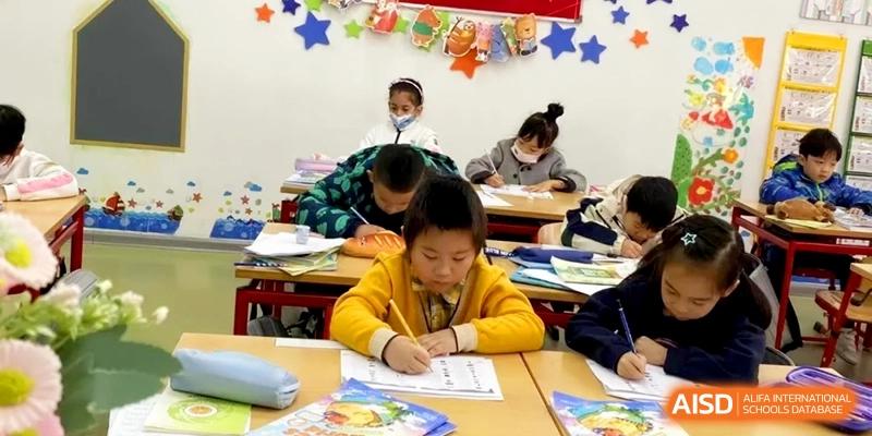 Students in colorful sweaters work diligently on their writing assignments in a bright classroom at Shanghai Gold Apple Bilingual School.