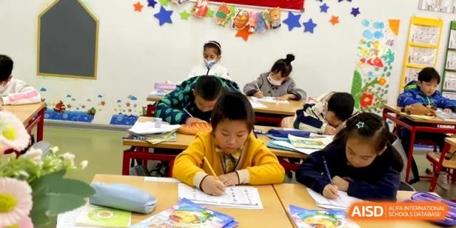 Students in colorful sweaters work diligently on their writing assignments in a bright classroom at Shanghai Gold Apple Bilingual School.