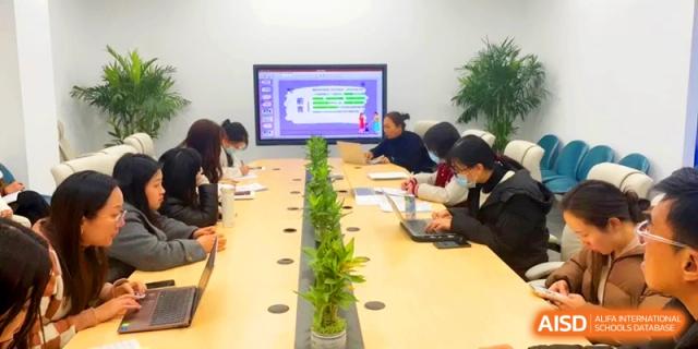 Faculty members hold a professional development meeting around a long table with plants at Shanghai Gold Apple Bilingual School.