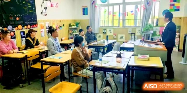 Adults sit in student desks while attending an observation or parent-teacher session at Shanghai Gold Apple Bilingual School.