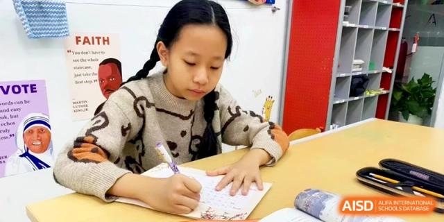 A young girl focuses intently while writing in her notebook during a lesson at Shanghai Gold Apple Bilingual School.