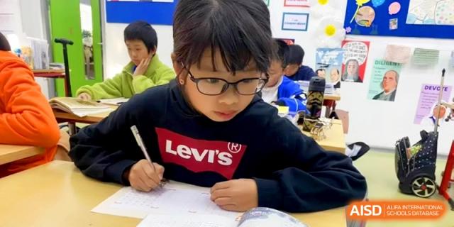 A boy wearing glasses concentrates on his schoolwork while writing at his desk at Shanghai Gold Apple Bilingual School.