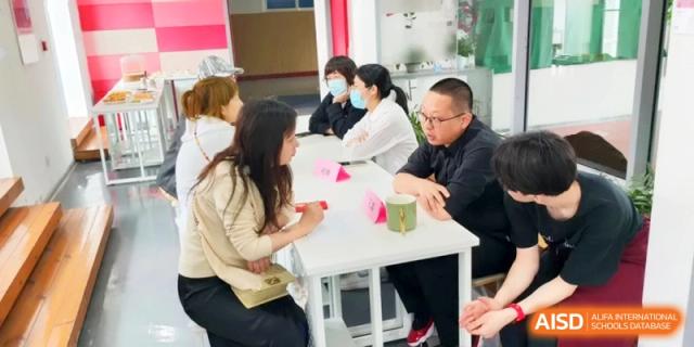 Parents and teachers engage in a collaborative meeting around a white table in a bright room at Shanghai Gold Apple Bilingual School.
