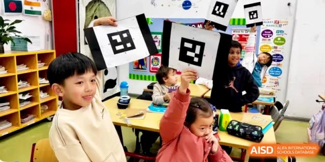 Smiling children enthusiastically hold up coded cards for a digital learning activity at Shanghai Gold Apple Bilingual School.