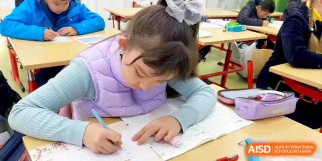 A young girl in a purple vest focuses on writing carefully in her workbook during class at Shanghai Gold Apple Bilingual School.