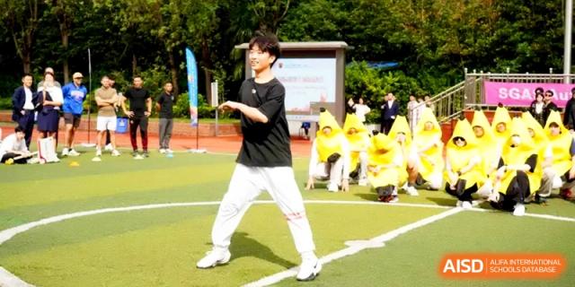 A student in a black shirt and white pants performing a dance routine on a green sports field at Shanghai Gold Apple Bilingual School.