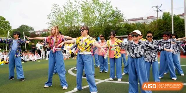 Students in colorful floral shirts and blue jeans performing a choreographed dance outdoors at Shanghai Gold Apple Bilingual School.