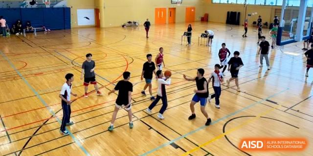 Students playing basketball on an indoor wooden court during a physical education session at Shanghai Gold Apple Bilingual School.
