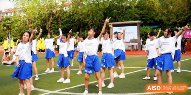 A group of students in blue and white uniforms performing a synchronized dance on the field at Shanghai Gold Apple Bilingual School.