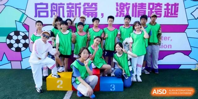 Students wearing green athletic vests posing together on a winner's podium during a sports event at Shanghai Gold Apple Bilingual School.