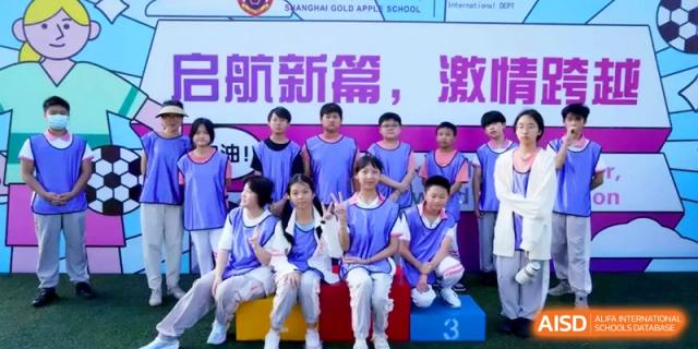 Students in blue sports vests pose on a tiered winner's podium during a ceremony at Shanghai Gold Apple Bilingual School.