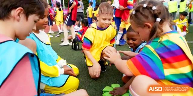 A young student in a yellow and rainbow-sleeved shirt focuses on a task outdoors at Shanghai Gold Apple Bilingual School.