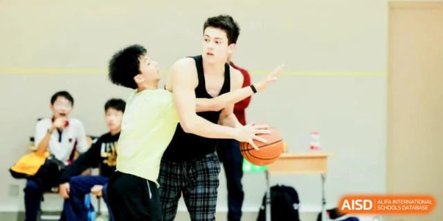 Two students compete for the ball during an intense basketball game on the indoor court at Shanghai Gold Apple Bilingual School.