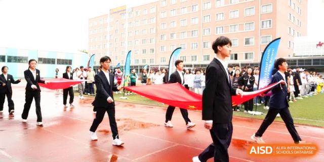 Students in formal suits carry a large flag during a ceremony on the school running track at Shanghai Gold Apple Bilingual School.