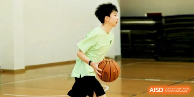 A student in a light green shirt focuses on dribbling a basketball during practice at Shanghai Gold Apple Bilingual School.