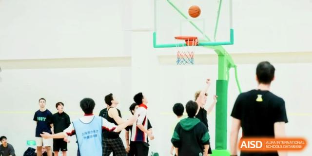 Several students watch as a basketball flies toward the hoop during an indoor match at Shanghai Gold Apple Bilingual School.