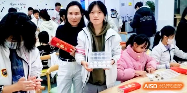 Two students proudly display a box of handmade dumplings and festive red scrolls at Shanghai Gold Apple Bilingual School.