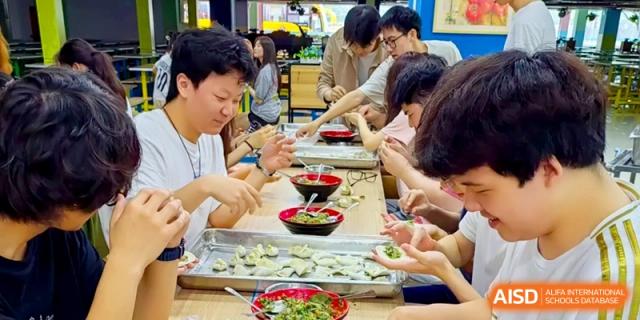 Students sitting at a long table focus on folding dumplings from trays of dough and filling at Shanghai Gold Apple Bilingual School.