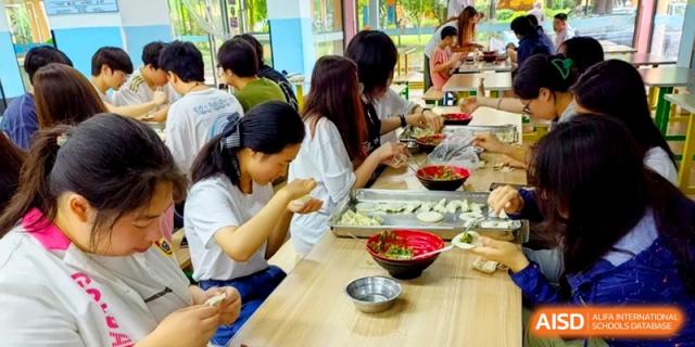 A young woman carefully folds a dumpling while her classmates work alongside her in a bright cafeteria at Shanghai Gold Apple Bilingual School.