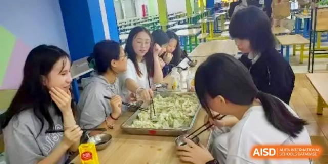 Students use chopsticks to arrange and pick up finished dumplings from a communal tray during a cooking activity at Shanghai Gold Apple Bilingual School.