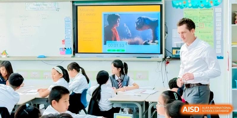 A classroom setting showing students at their desks focused on a large digital screen displaying a film scene during a lesson at Shanghai Qingpu World Foreign Language High School.
