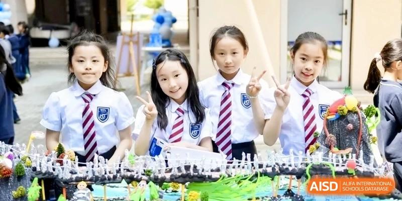 Two young students in striped ties and white uniforms smile and pose with peace signs behind a school project display at Shanghai Qingpu World Foreign Language High School.