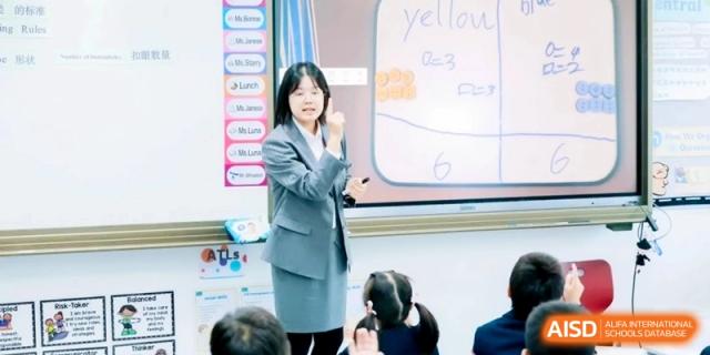 A female teacher in a grey suit points to a whiteboard while instructing a classroom of students at Shanghai Qingpu World Foreign Language High School.