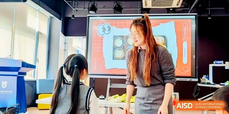 A teacher with long reddish hair stands by a digital whiteboard, engaging with a student during an interactive classroom activity at Shanghai Qingpu World Foreign Language High School.